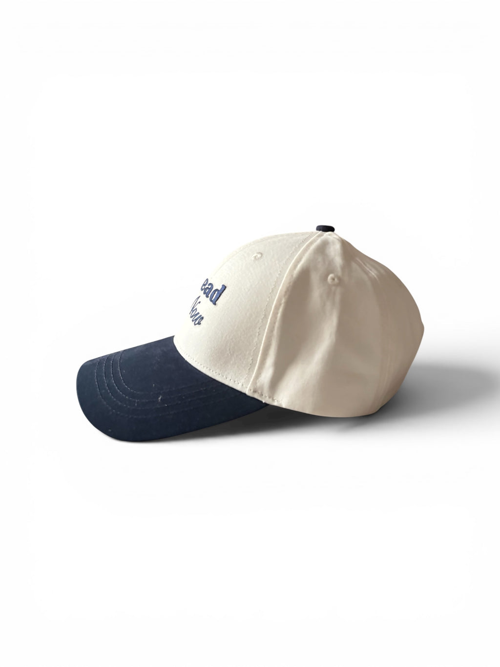 Cream and navy fashion cap, side view, showing Ahead of Now embroidery