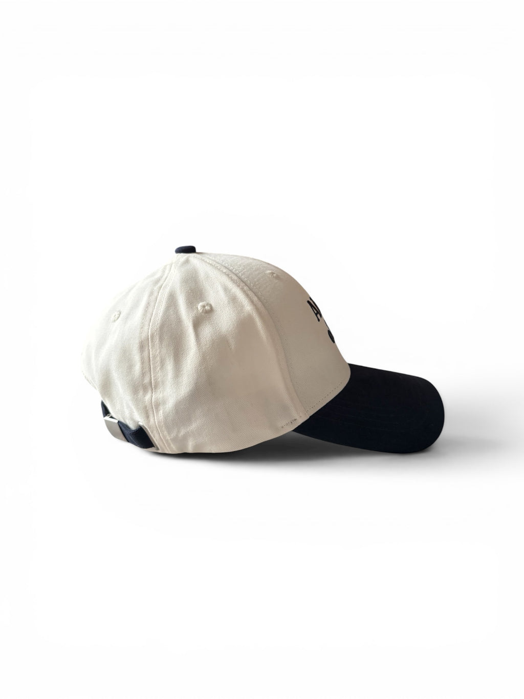 Cream and navy fashion cap, side view, showing embroidered logo and adjustable strap